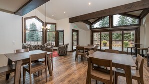 A spacious dining area with wooden tables and chairs, large windows with a view of trees, and a high ceiling with exposed beams. - Seasonal Pool and Year-Round Hot Tub (Sun Valley)