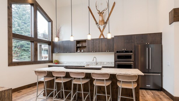 A modern kitchen with a large island, bar stools, a deer head mounted on the wall, and a large window. - Seasonal Pool and Year-Round Hot Tub (Sun Valley)