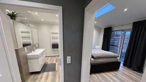 Un dormitorio moderno con cama, mesita de noche, ventana con cortinas y vistas al exterior.