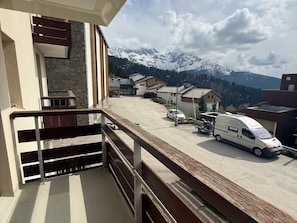 A balcony with a view of a parking area and snow-capped mountains in the background. - 2-room cabin apartment at the foot of the slopes with balcony (Les Adrets-Prapoutel)