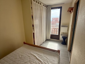 A bedroom with a bed, a window with curtains, a radiator, and a view of a building outside. - 2-room cabin apartment at the foot of the slopes with balcony (Les Adrets-Prapoutel)