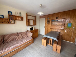 A compact living space with a wooden sofa, a small table, and shelves with books and decorative items. - 2-room cabin apartment at the foot of the slopes with balcony (Les Adrets-Prapoutel)