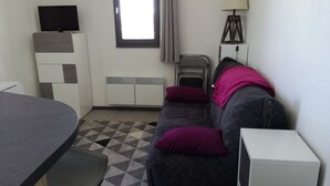 Ein gemütlicher Raum mit Schlafsofa, kleinem Tisch, Fernseher, Lampe und Fenster.