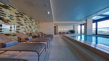 Un área de piscina interior moderna con sillones de descanso y una pared con diseño.