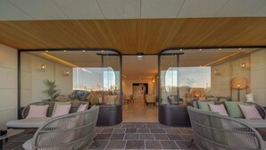 A modern lounge area with wicker furniture, a stone floor, and glass walls offering views of the cityscape. - Land's End Boutique Hotel (Sliema)