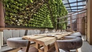 A modern dining area with a long wooden table set for six, surrounded by cushioned chairs, and a vertical garden wall behind. - Land's End Boutique Hotel (Sliema)