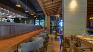 A restaurant interior with a long counter, bar stools, wooden tables, and hanging pendant lights.