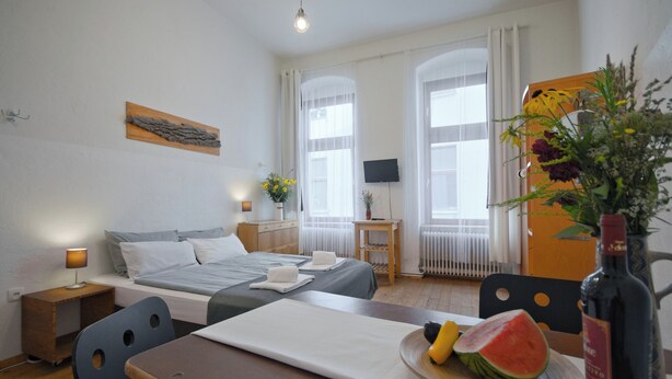 A hotel room with a bed, bedside table, lamp, and a dining area with a table, chairs, and a plate of fruit.
