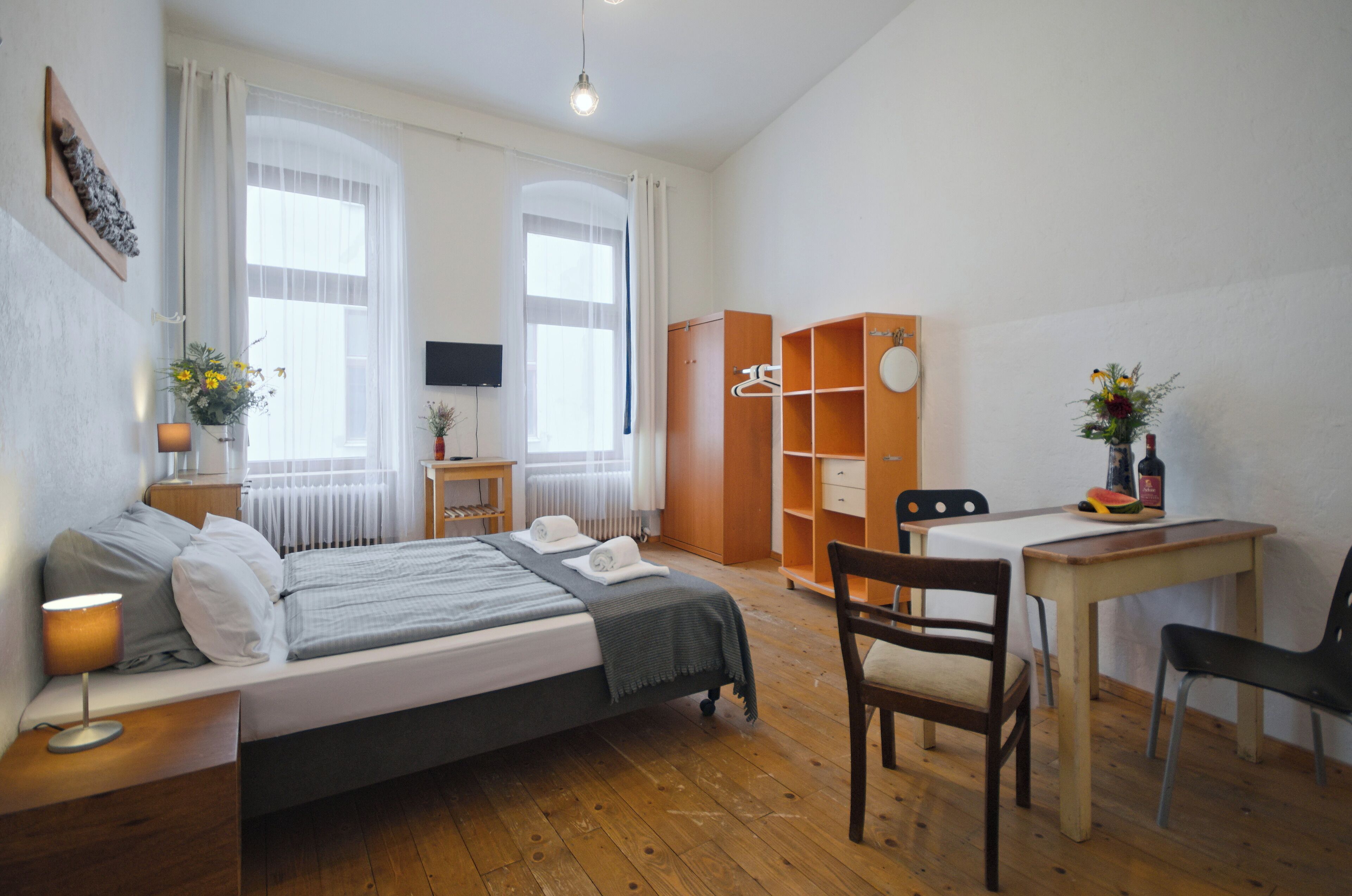 Een slaapkamer met een bed, nachtkastje, lamp, dressoir en een bureau met stoel.