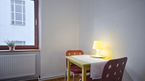 A small dining area with a table, two chairs, a lamp, and a window with a view of a building.