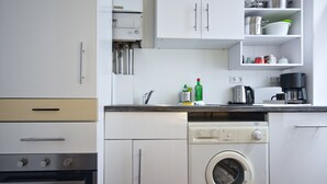 A compact kitchen with a built-in washer and dryer, a coffee maker, and a shelf with kitchenware.