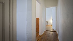 A hallway with wooden flooring and white walls, leading to a room with a wooden door.