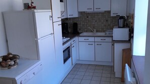 Een kleine keuken met witte kastjes, een koelkast, een koffiezetapparaat en een betegelde spatwand.