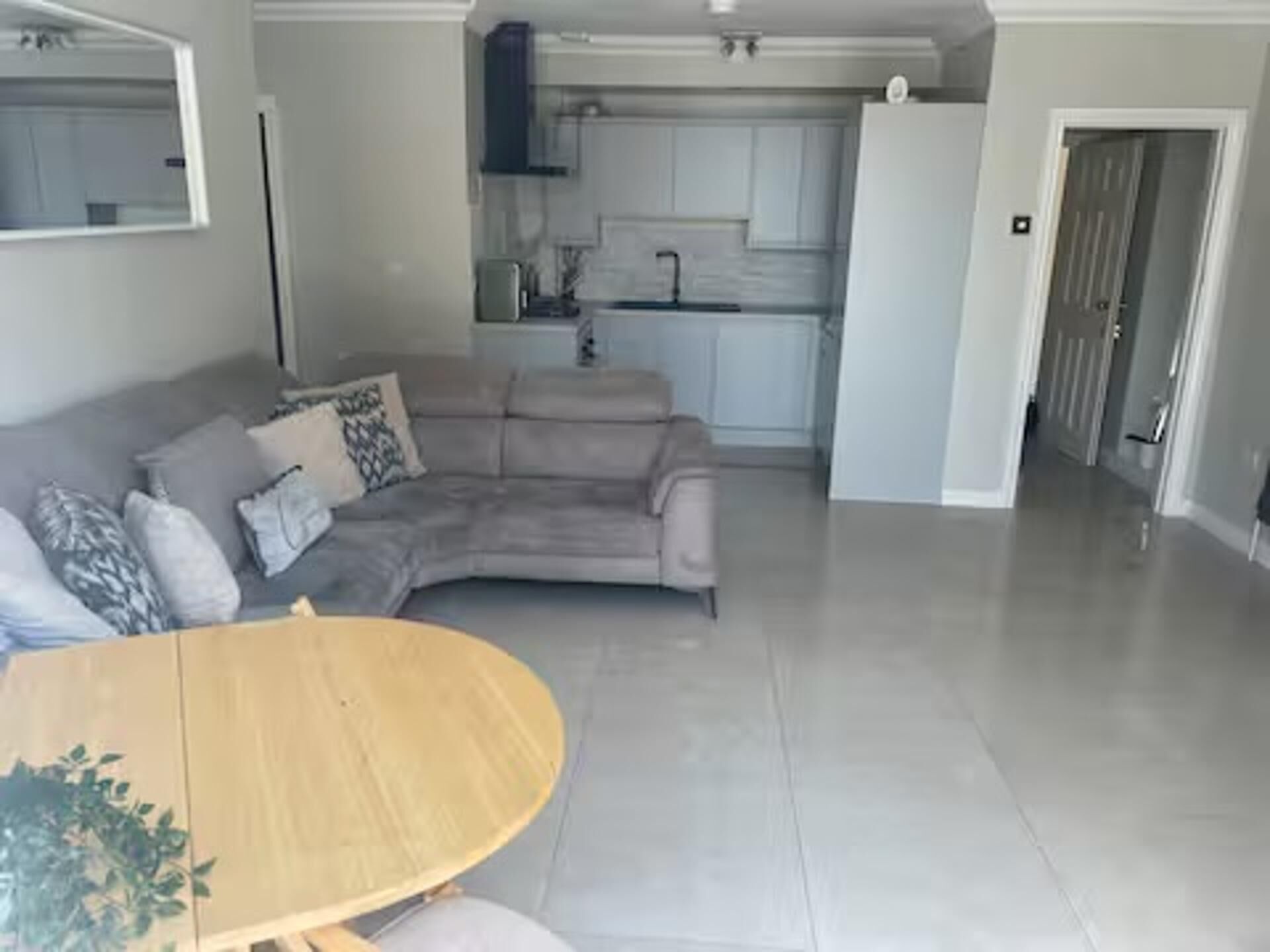 A living room with a grey sofa, a wooden table, and a kitchen in the background.