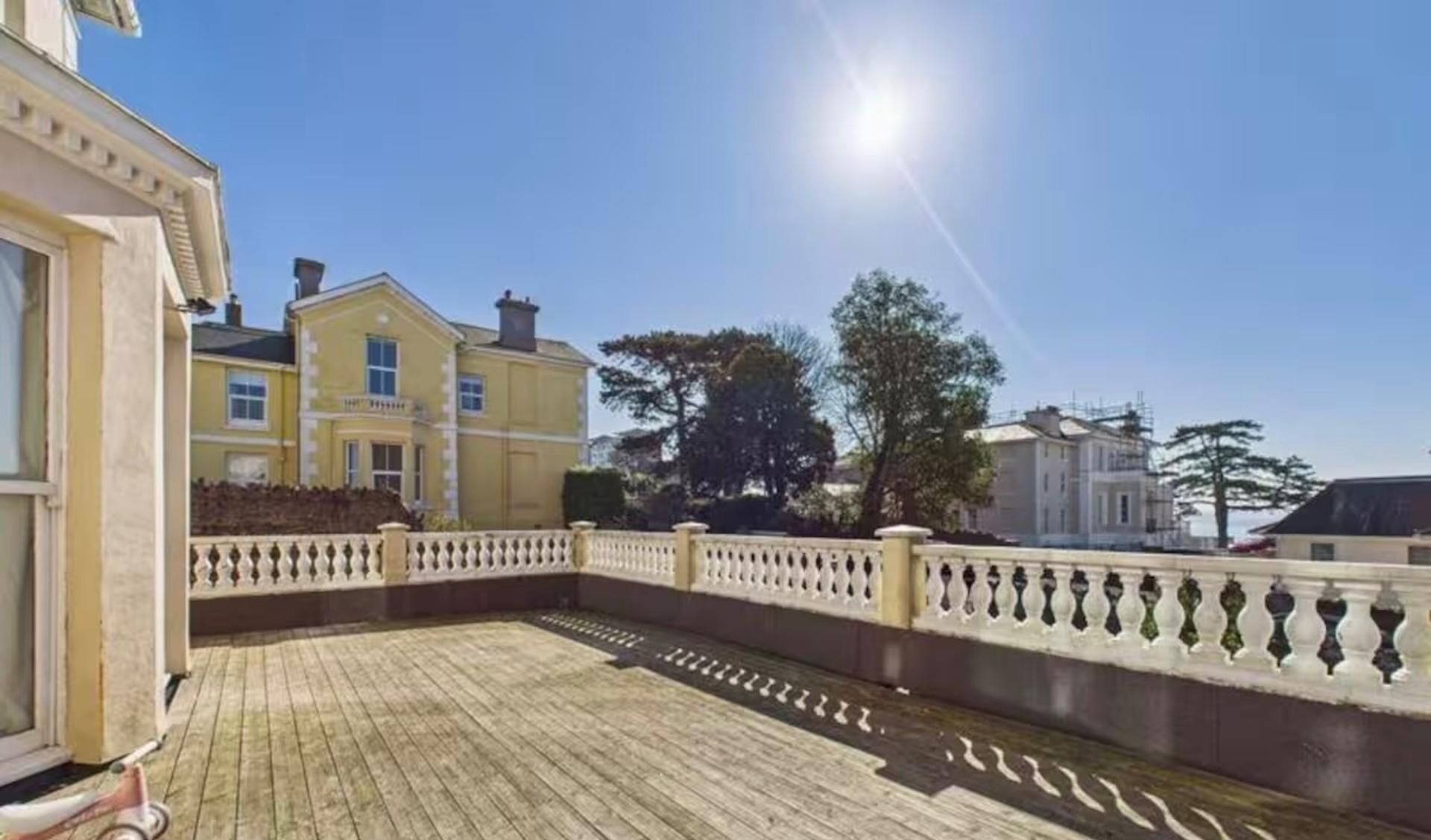 A courtyard with a wooden deck, a white balustrade, and buildings in the background.