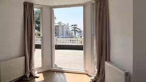 Habitación de hotel con una ventana grande, un radiador y vistas a un edificio y árboles.