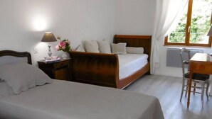 Ein Schlafzimmer mit zwei Betten, einem Nachttisch mit Lampe, einem Sessel und einem Fenster mit Vorhängen.