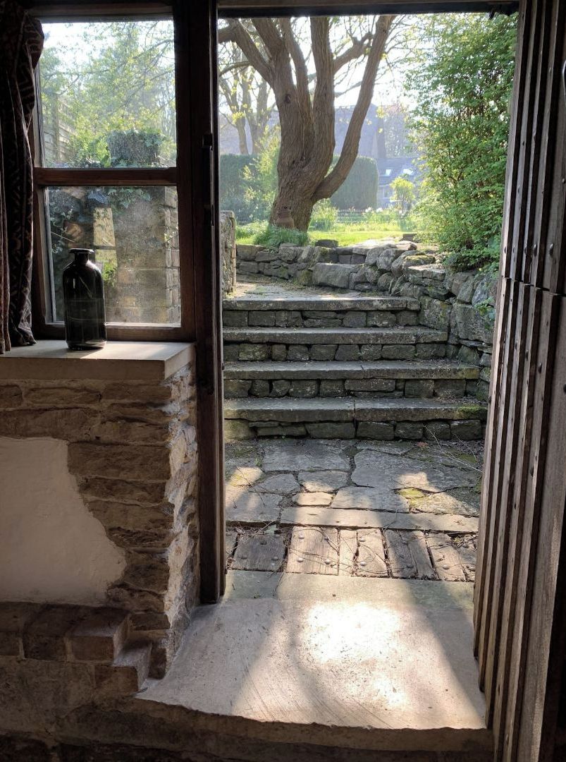 A stone staircase leading outside, a window with a vase on the windowsill, and a view of a tree-lined garden.