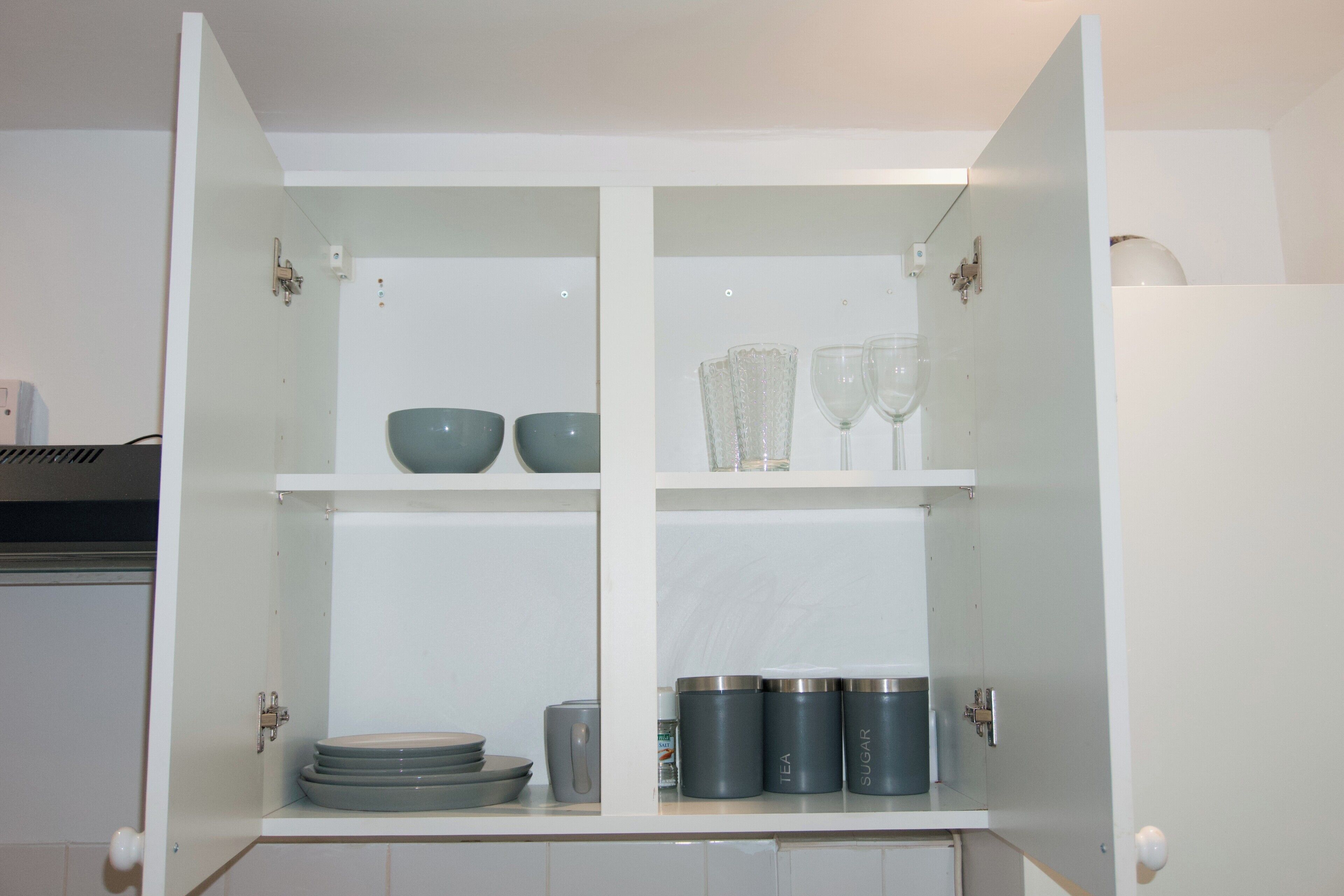 A kitchen cabinet with shelves containing bowls, glasses, and containers labeled 'TEA' and 'SUGAR'.