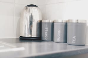 Una encimera de cocina con un hervidor y tres recipientes etiquetados como café, azúcar y té.
