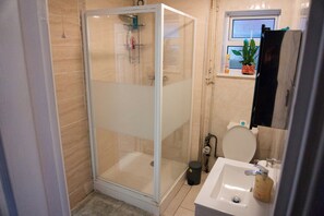 Un baño con ducha de vidrio, inodoro, lavamanos y ventana con planta.