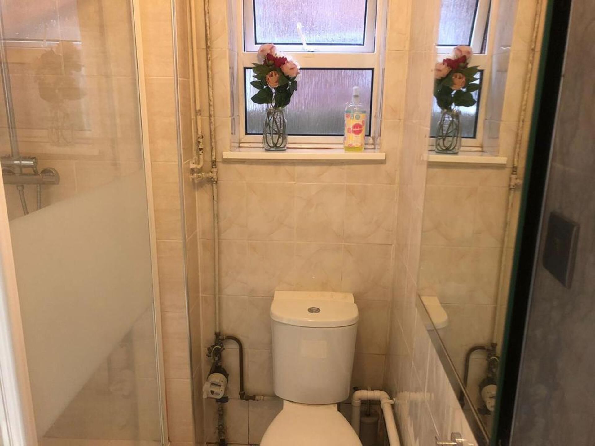 Et badeværelse med toilet, et vindue med blomster og en bruseplads.