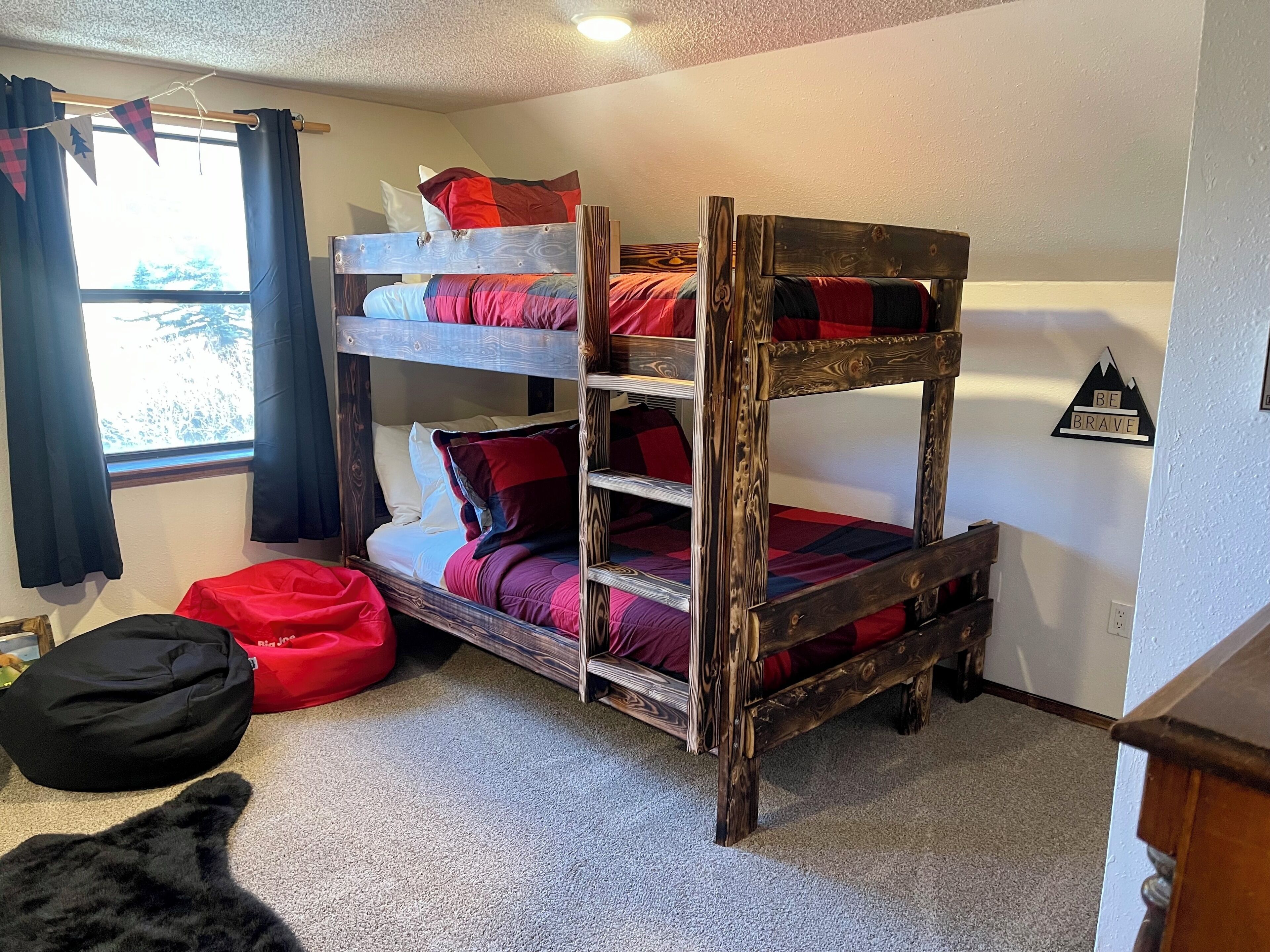 Une chambre avec un lit superposé, une fenêtre, un panneau motivant accroché au mur et un pouf rouge en forme de haricot.