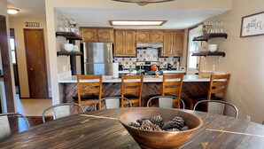 Una cocina con armarios de madera, un refrigerador de acero inoxidable y un comedor con mesa y sillas de madera.