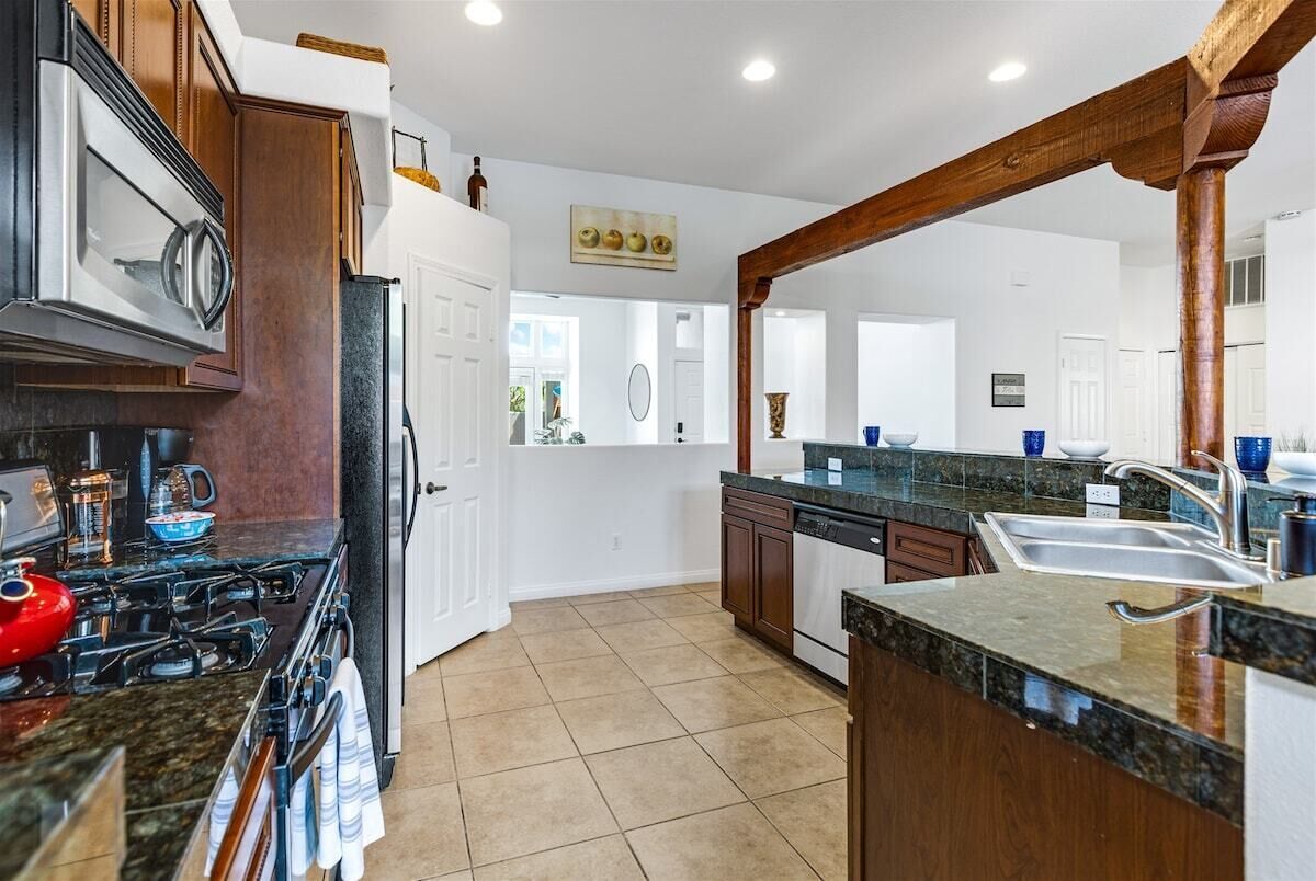 A modern kitchen with granite countertops, a stainless steel range, and a wooden archway.