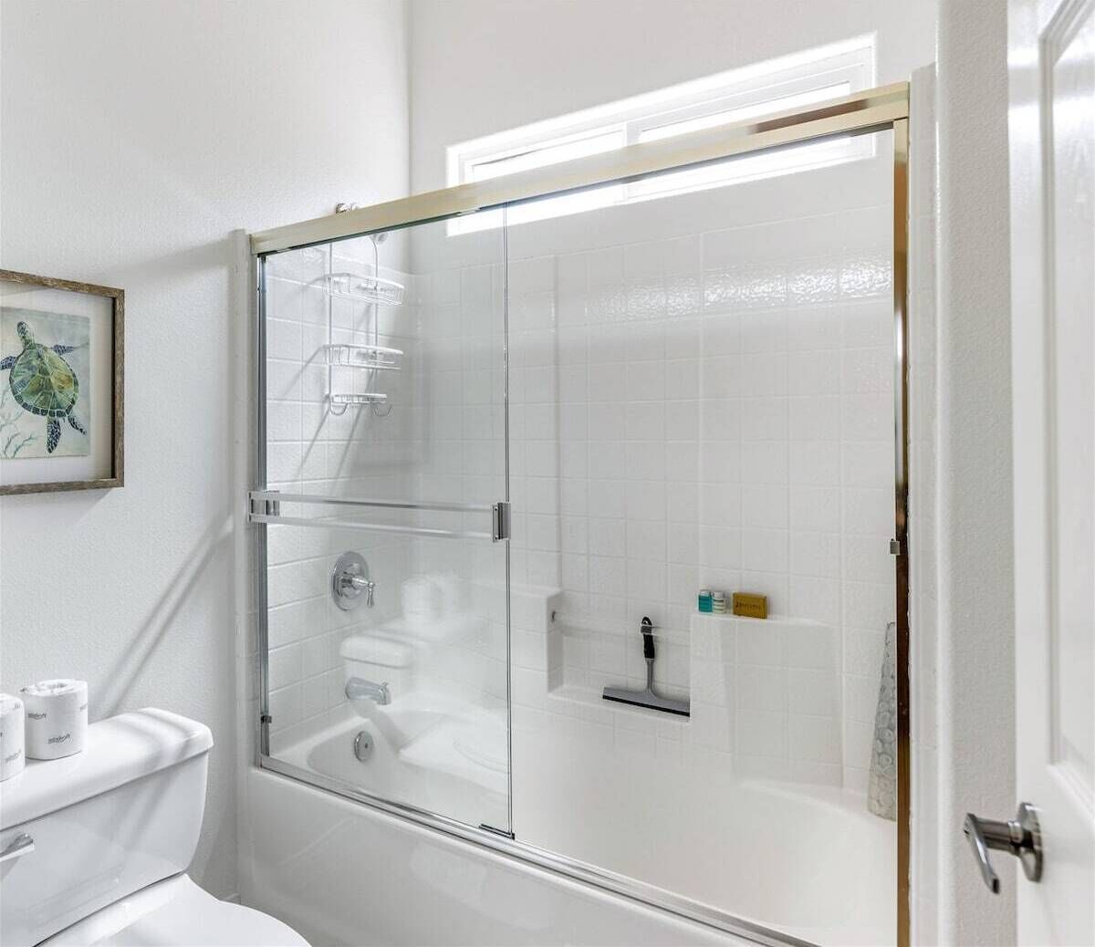 A modern bathroom with a glass-enclosed shower, white tiles, and a framed picture on the wall.