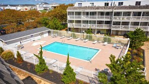 Ein Pool mit Liegestühlen und einem umzäunten Deckbereich, umgeben von Bäumen und einem Gebäude mit Balkonen.