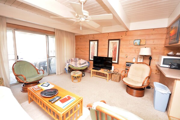 A cozy living room with a television, wicker chairs, a wooden floor, and a balcony with curtains. - 3 Bedroom Townhouse with Free WiFi, an Outdoor Pool, and Sand for kids to play in located just steps from the beach in midtown! (OCEAN CITY)