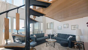 Ein modernes Wohnzimmer mit großem Fenster, einer Sofagarnitur, einem Couchtisch und einer Treppe mit Meerblick.