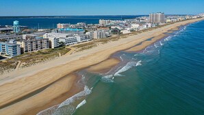 Luchtbeeld van een kustplaats met een breed strand, gebouwen en een helderblauwe lucht.