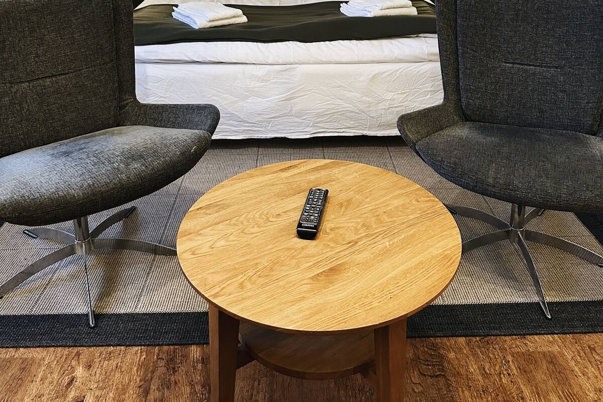 A hotel room with a bed, two nightstands with lamps, a round wooden table, and two armchairs.