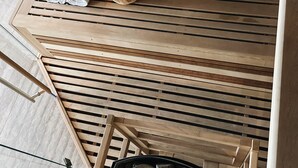 Una sauna de madera con un banco, una toalla, un cuenco de madera y un calentador de sauna.