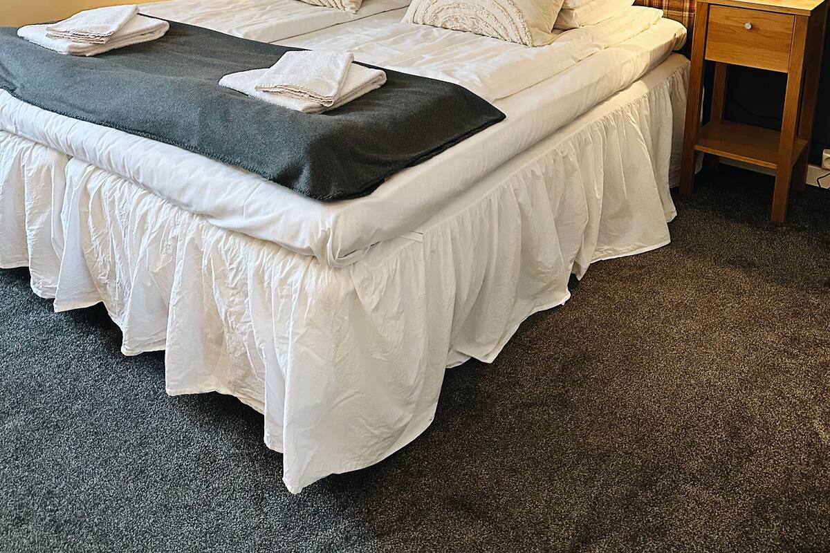 A neatly made bed with white linens and a dark throw blanket, flanked by two bedside tables with lamps, in a room with dark walls and a framed picture above the bed.