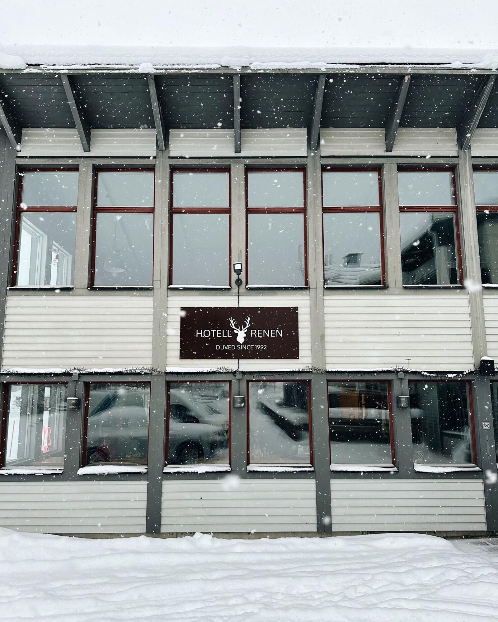 A hotel building with multiple windows, a signboard, and snow on the roof.