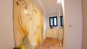 Un couloir agrémenté d’un mur décoratif, d’un sol carrelé et d’un coin cuisine avec des placards et une fenêtre.