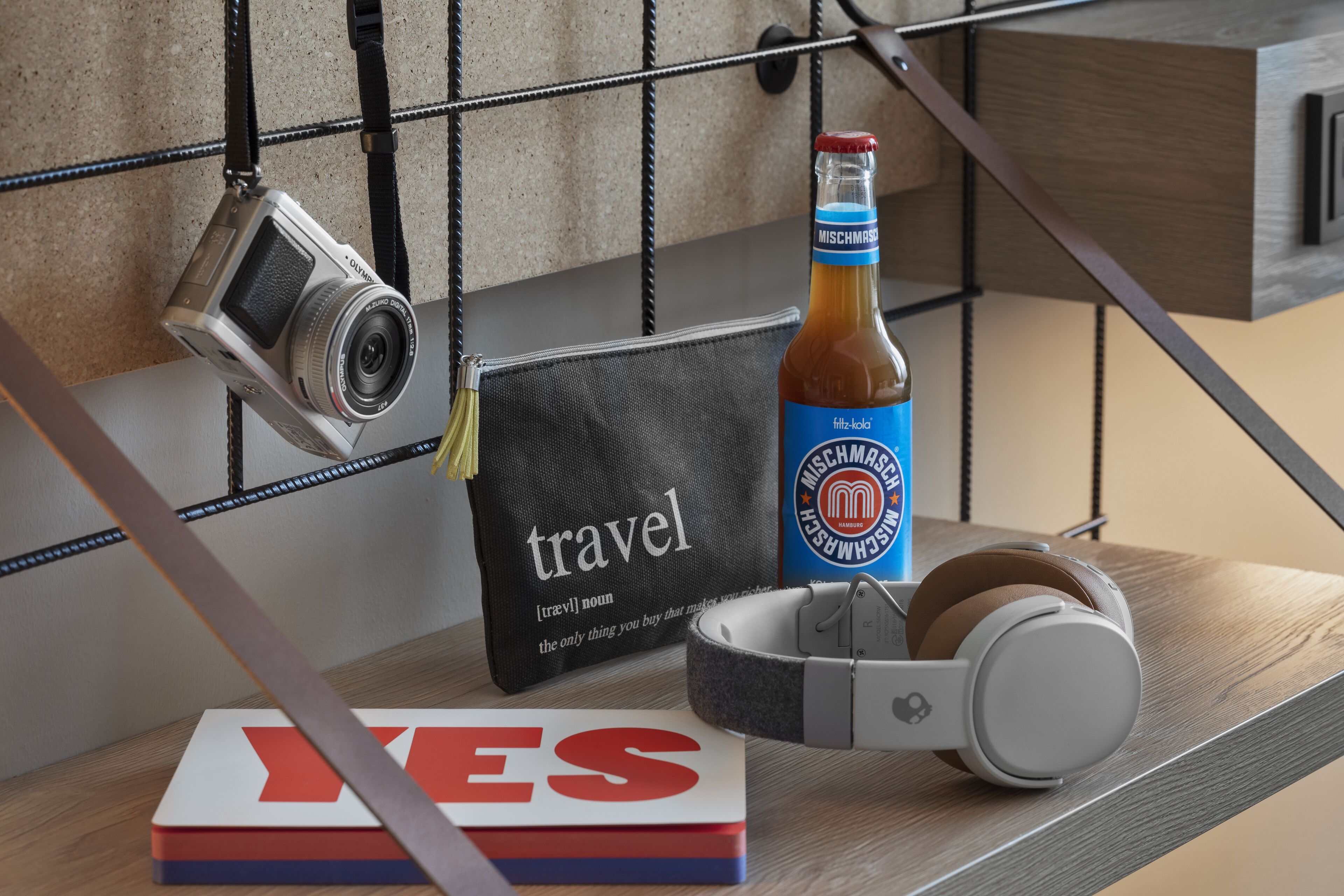 A camera, a bottle, headphones, and a book on a wooden surface.