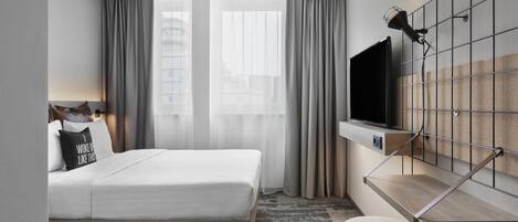 Una habitación de hotel moderna con cama, televisión montada en la pared, una mesita y una ventana con cortinas.
