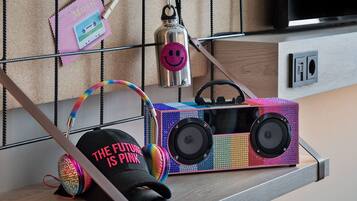 A room with a wooden shelf holding a colorful boombox, a pair of headphones, a cap, and a small bottle.