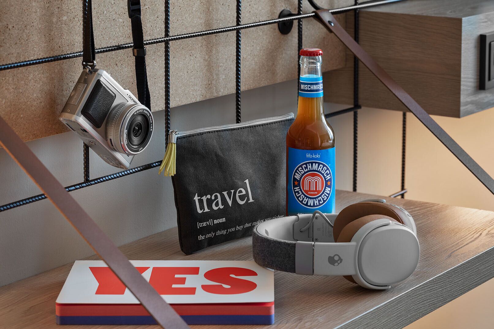 A travel-themed setup with a camera, a bottle of Mischnash beer, headphones, and a book with the word 'YES' on a wooden surface.