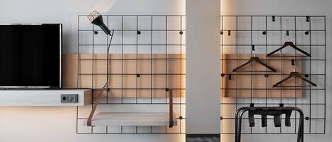 A modern room with a mounted TV, a light fixture, a shelf, a hanging rack, and a bench.