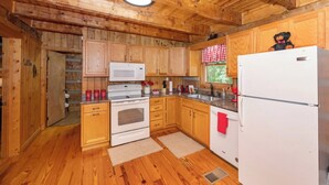 A wooden cabin kitchen with a white stove, microwave, and refrigerator. - Cozy Cabin - Large Yard w/ Firepit, walk to Fishing Pond, Pool, & Mini Golf (Sevierville)