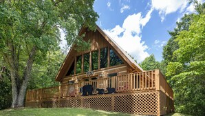 A wooden cabin with a balcony, surrounded by trees. - Cozy Cabin - Large Yard w/ Firepit, walk to Fishing Pond, Pool, & Mini Golf (Sevierville)