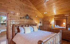 A wooden cabin bedroom with a large bed, a dresser, and a mirror.