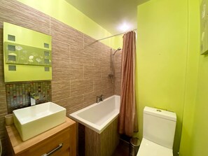 Une salle de bain avec une grande baignoire blanche, des toilettes blanches et un meuble-lavabo en bois avec un miroir.