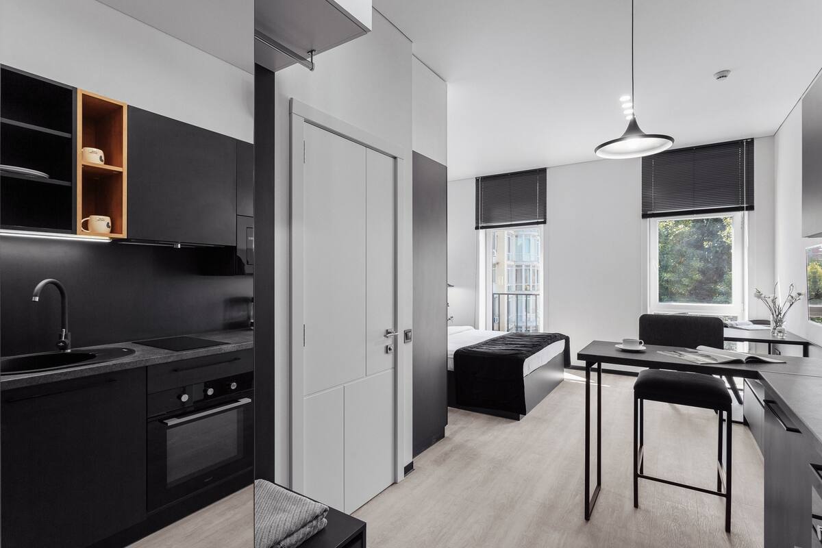 A modern kitchen with a built-in oven, a dining area with a bar stool, and a view of the outdoors through large windows.