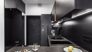 A modern kitchen with dark cabinetry, a built-in sink, and a countertop with a magazine, a glass of water, and a plate with lemons. - WOL 121 (Odesa)